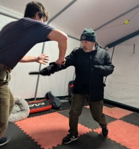 A martial arts instructor intercepts and jams an incoming knife attack from a training partner, controlling the weapon arm at close quarters.